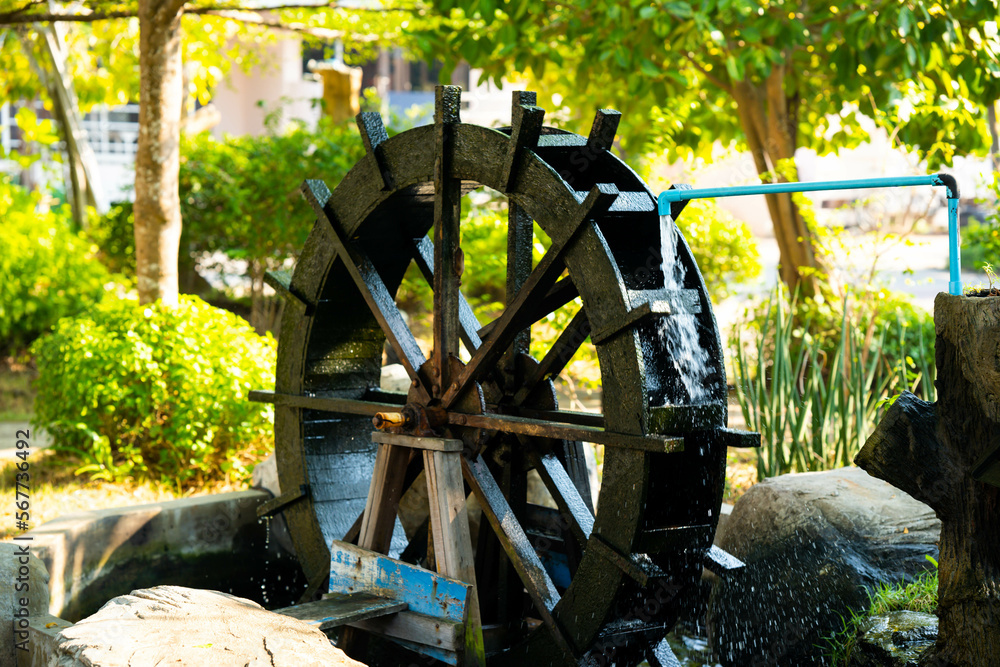 A working watermill wheel with falling water on a background of green trees on a clear sunny day
