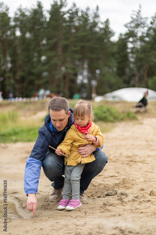 Fototapeta premium Little girl drawing on sand with her father