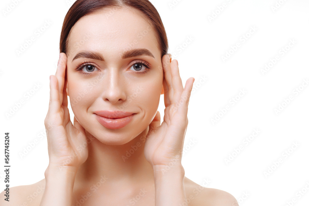 Young brunette woman with flawless skin and bare shoulders on a white background holds her hands near her face. The concept of skin care and spa treatments, self-care and anti-aging beauty treatments.