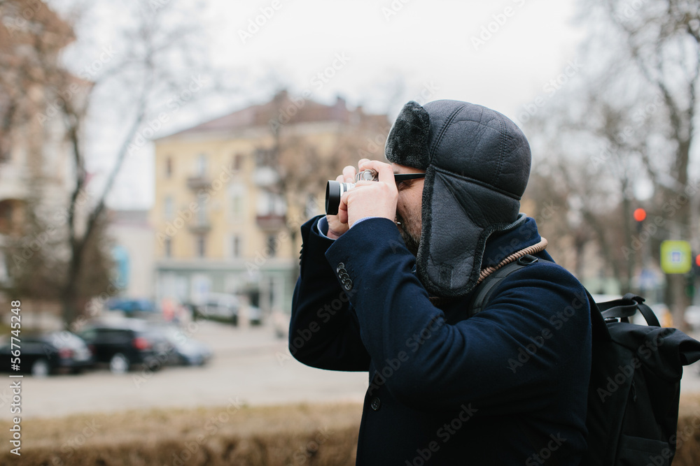 A senior tourist takes pictures of the winter city on his film camera. Travel and hobby concept.