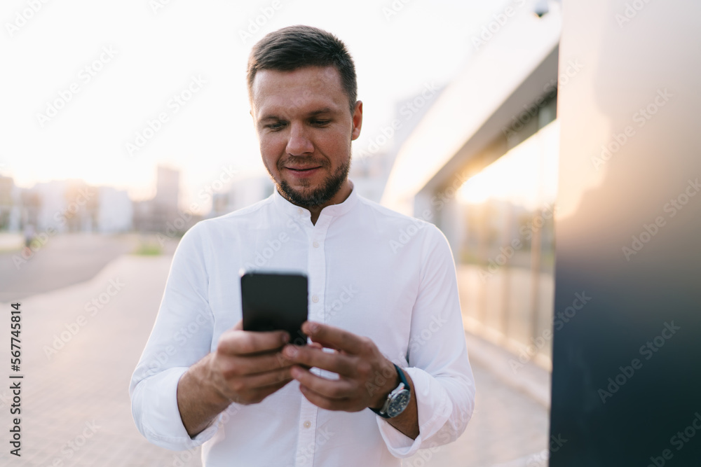 Smiling man looking at screen of smartphone while standing on street Smiling man looking at screen of smartphone while standing on street