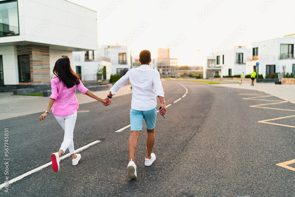 Unrecognizable couple holding hands and running on asphalt road Unrecognizable couple holding hands and running on asphalt road