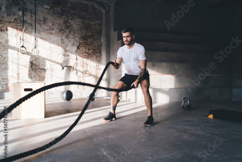 Strong man doing exercises with battle ropes in gym