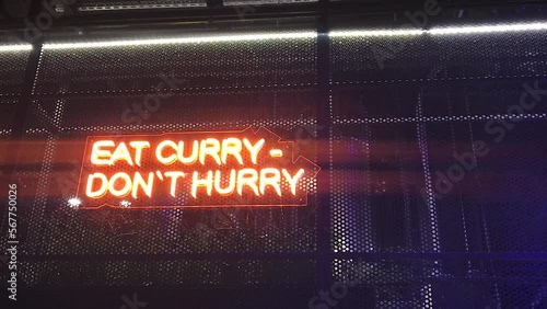 Neon inscription eat curry don't hurry,attracting visitors to Indian food cuisine,red orange color, flickers glows in the dark wall of the restaurant.indoors night.concept food court neon signage. photo