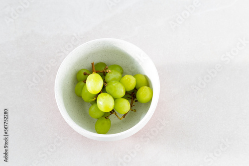 Selective focus flat lay side lit view of green grapes in white lightly speckled bowl on ceramic background