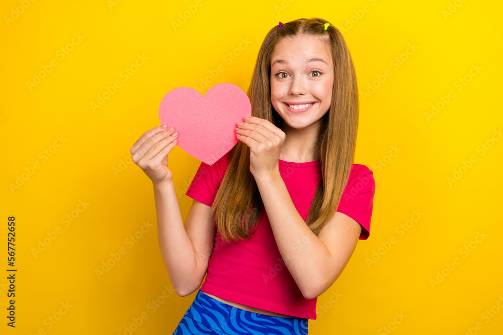 Photo of youngster teen age girl wear pink t-shirt crop top hold paper pink love symbol feelings first boyfriend isolated on yellow color background Photo of youngster teen age girl wear pink t-shirt crop top hold paper pink love symbol feelings first boyfriend isolated on yellow color background
