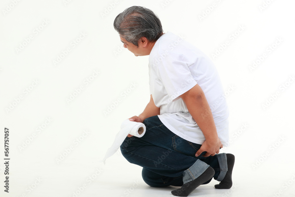 Asian fat man sitting on white floor holding toilet paper He used his other hand to hold his buttocks. The concept of health care for obese people. hemorrhoids Asian fat man sitting on white floor holding toilet paper He used his other hand to hold his buttocks. The concept of health care for obese people. hemorrhoids