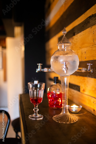 Close up of a traditional ornate absinthe  fountain with a glass and bottle of red liqueur photo