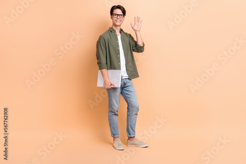 Full body size cadre of young friendly guy worker copywriter hold netbook palm hello office employee wear glasses isolated on beige color background