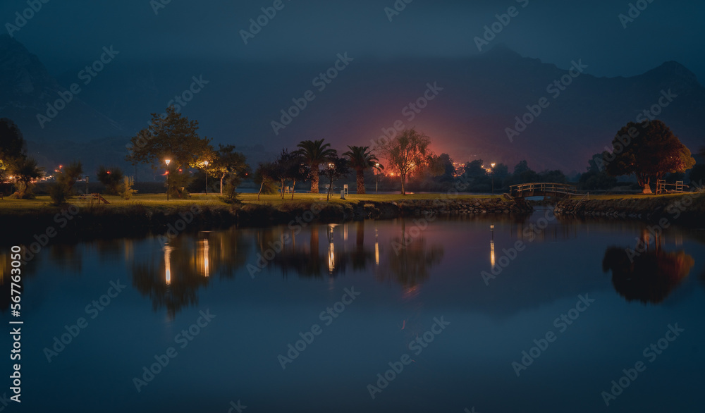 Family park at night with some streetlght lightning it and reflecting on river.