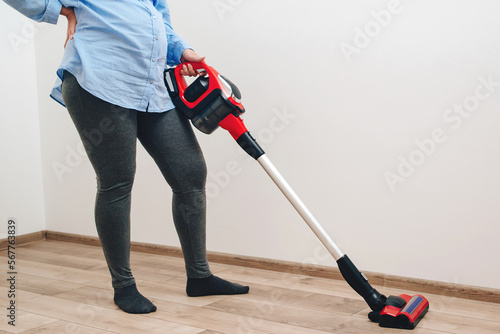 Young pregnant woman enjoys cleaning her house. Modern easy cleaning. Easy cleaning with a wireless vacuum cleaner.