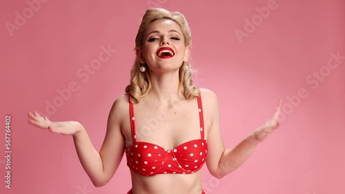La la la. Positive vibe. Beautiful young blonde girl with retro hairstyle in swimming suit over pink studio background. Concept of retro fashion, beauty, attraction, 50s, 60s. Pin-up style. Vintage photo