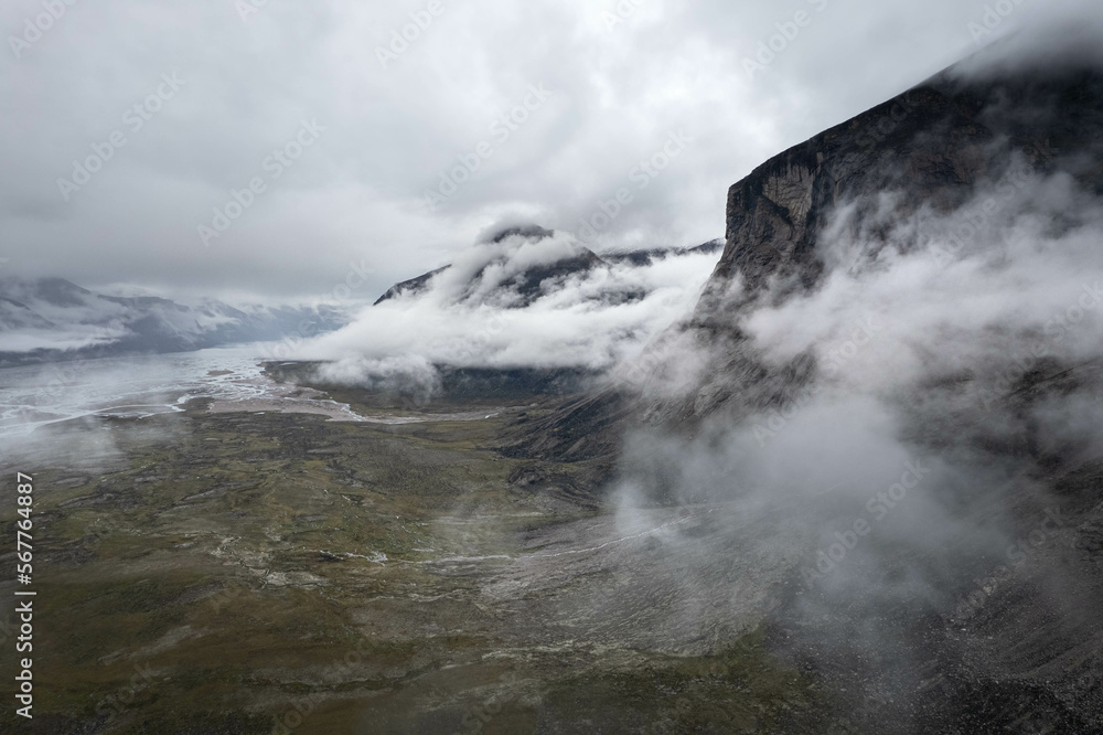 Scienic landscape with rocky mountain top in low clouds in gray cloudy sky. Akshayuk Pass, Baffin Island mountain seen through clouds. mountains background