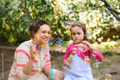 Selective focus on soap bubbles on blurred background of a happy mom and daughter having fun together in the back yard