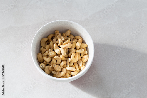 Selective focus flat lay side lit view of cashew nuts in lightly speckled white bowl on ceramic background