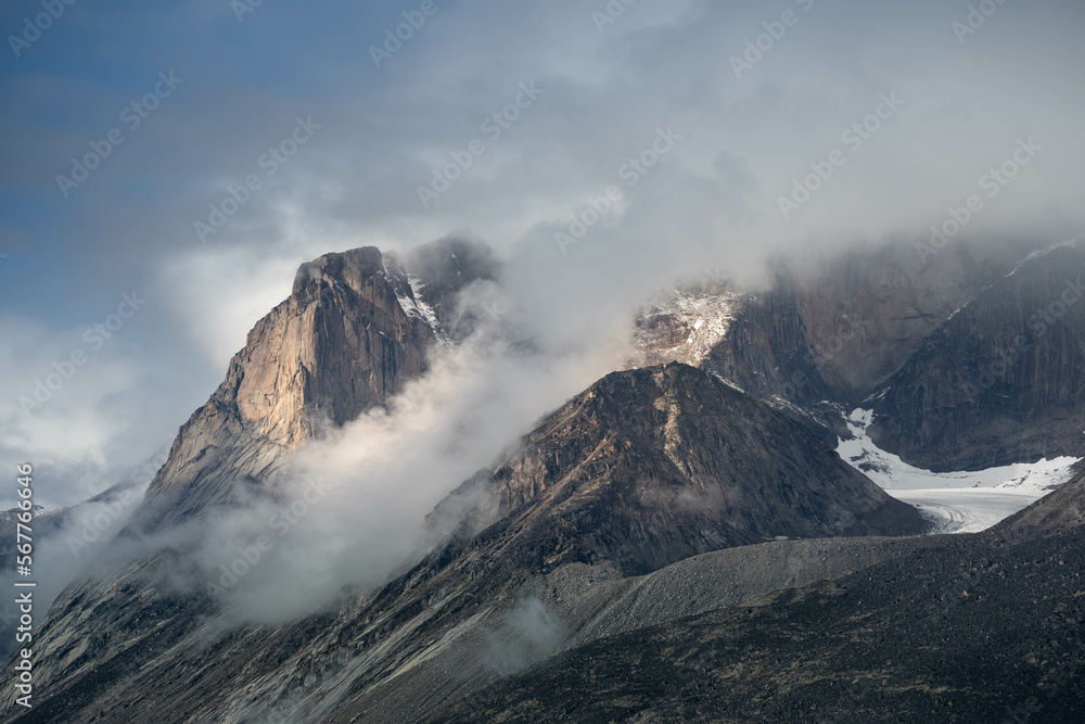 Scienic landscape with rocky mountain top in low clouds in gray cloudy sky. Akshayuk Pass, Baffin Island mountain seen through clouds. mountains background