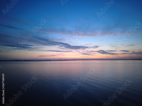 Beautiful sunset on the Baltic Sea with blue sky and clouds, colorful sky reflected in the water. Coast of Denmark on the horizon at summer twilight evening