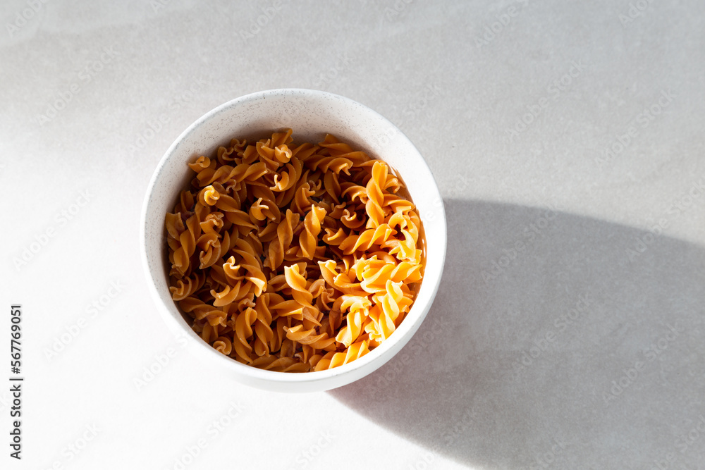 Selective focus flat lay side lit view of uncooked pasta torsades in lightly speckled white bowl on ceramic background Selective focus flat lay side lit view of uncooked pasta torsades in lightly speckled white bowl on ceramic background