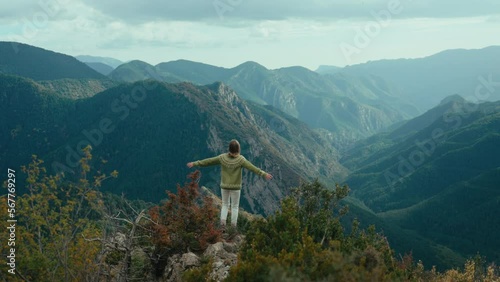 Cinematic woman in traditional sweater hike in mountain. Female hiker reach top of the hill, spread and raise hands in excitement and success. Freedom and joy of travel and outdoor lifestyle.