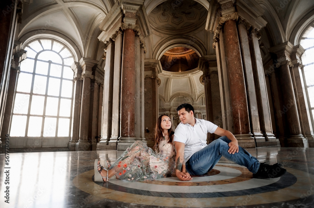 Naklejka premium A young couple is hugging in the hall of a large historic building. Tender relations between a man and a woman. A walk in historical places. Good weather for a walk. Meeting and excursion.