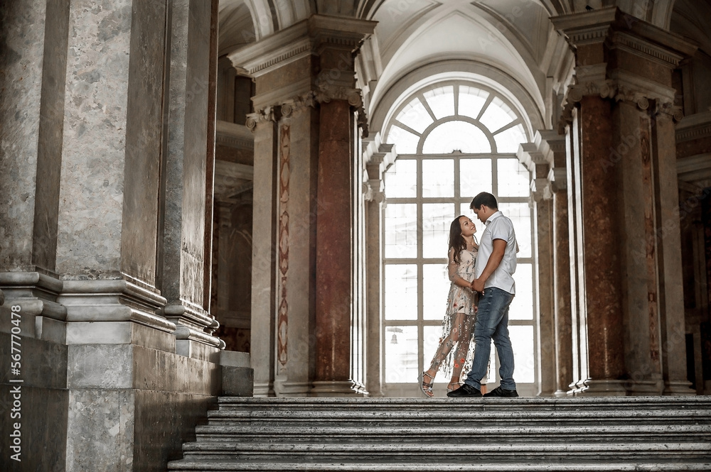 A young couple is hugging in the hall of a large historic building. Tender relations between a man and a woman. A walk in historical places. Good weather for a walk. Meeting and excursion.
