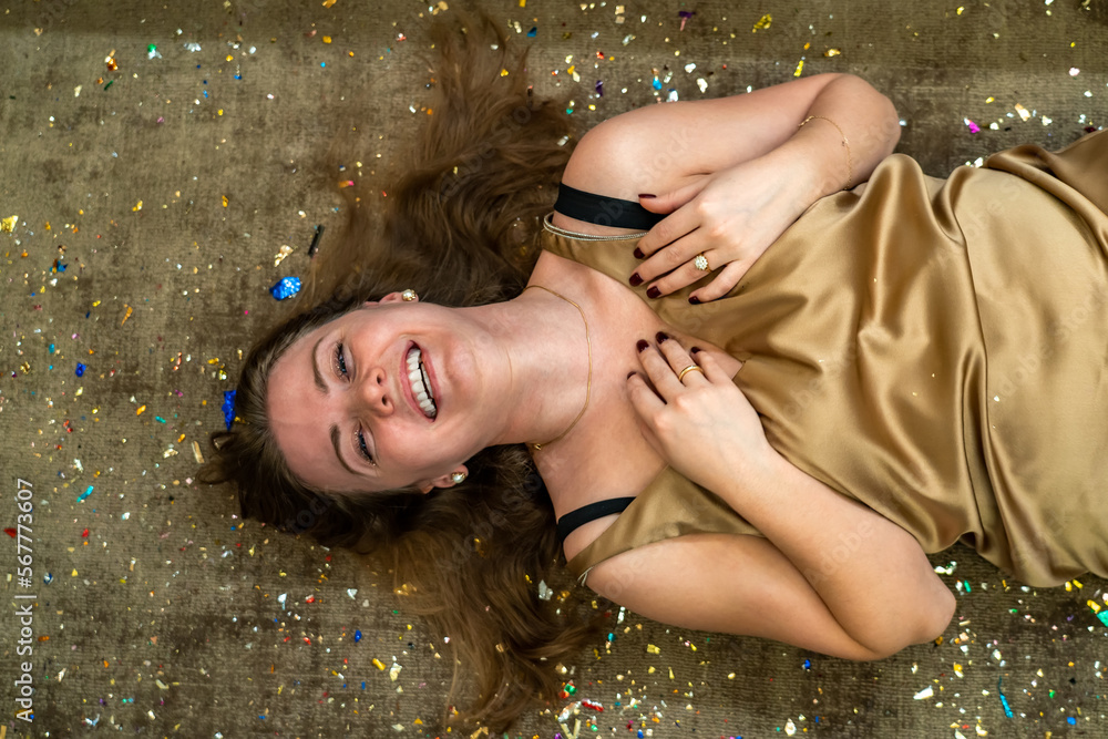 Obraz premium Carefree laughing lady in golden dress lying on floor among confetti