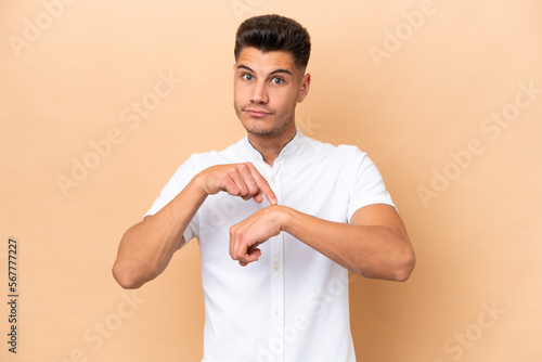 Young caucasian man isolated on beige background making the gesture of being late