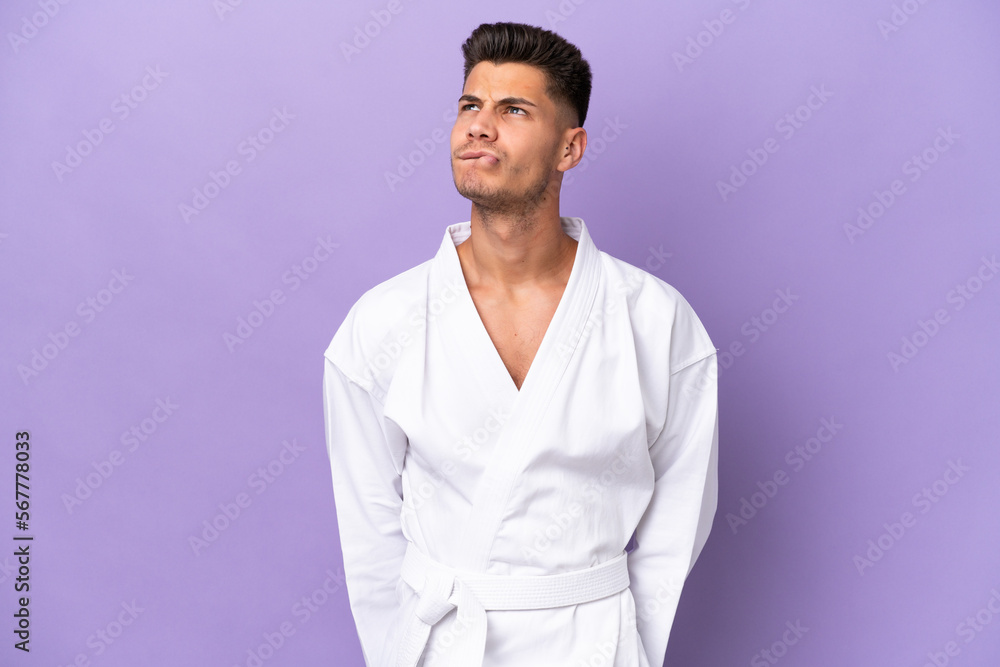 Young caucasian man doing karate isolated on purple background and looking up Young caucasian man doing karate isolated on purple background and looking up