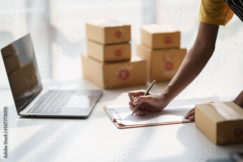 Asian female online business owner writing customer's details on document.