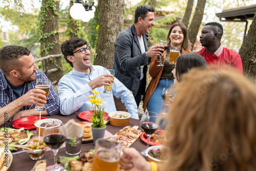 Family and friends enjoying a lunch at home  young multiracial people drinking beer at barbecue party in backyard restaurant patio  concept about friends enjoying time together
