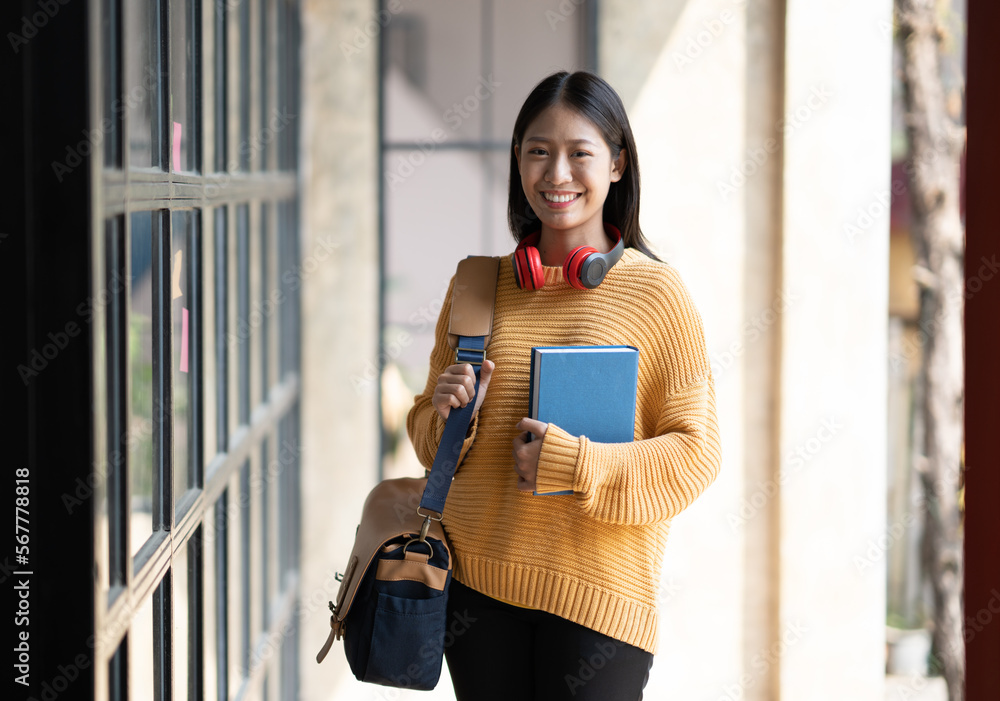 Young Asian Student Standing at Entrance to University Building. Getting rady to go to classroom holding books and bag. - obrazy, fototapety, plakaty 