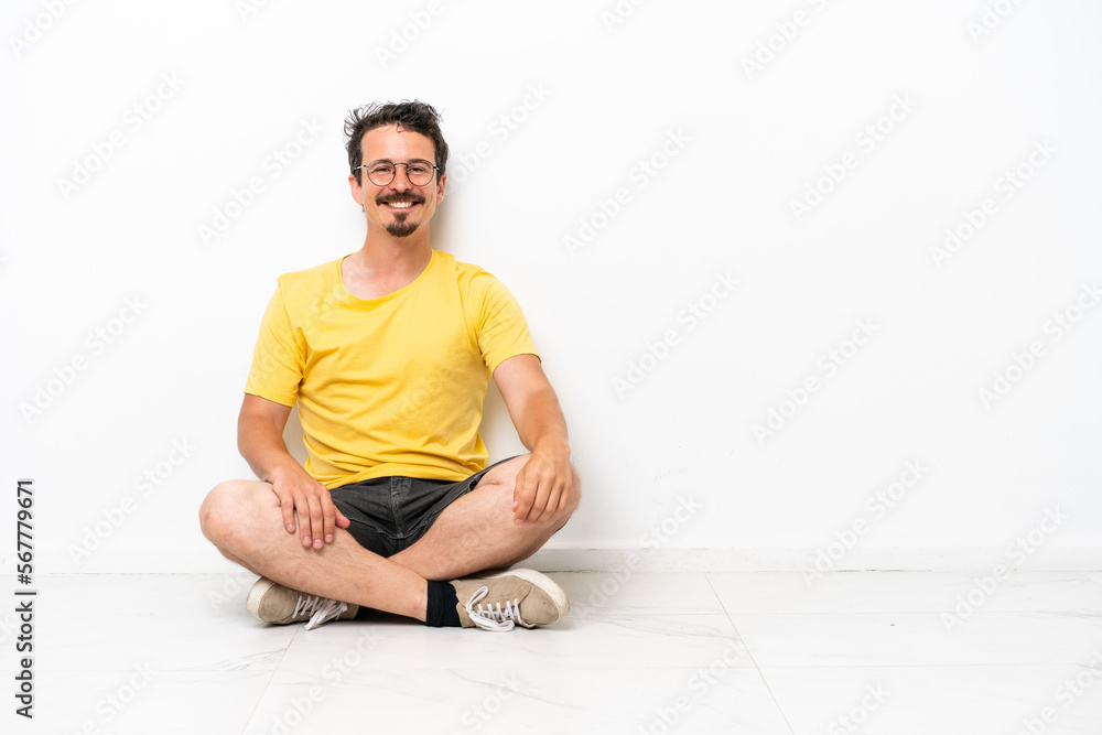 Fototapeta premium Young caucasian man sitting on the floor isolated on white background laughing