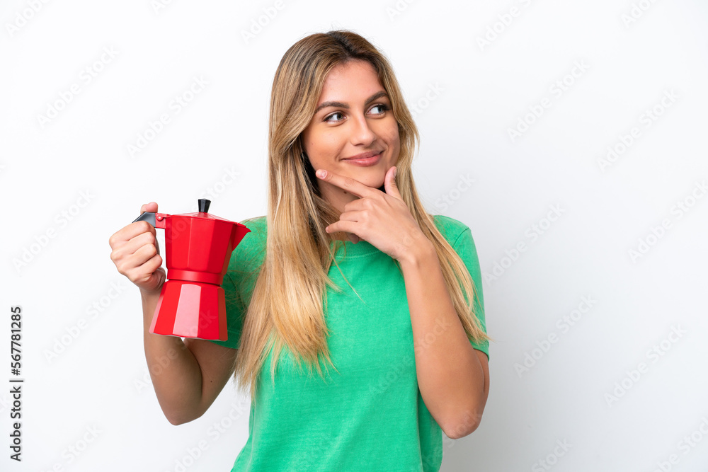 Young Uruguayan woman holding coffee pot isolated on white background thinking an idea and looking side Young Uruguayan woman holding coffee pot isolated on white background thinking an idea and looking side