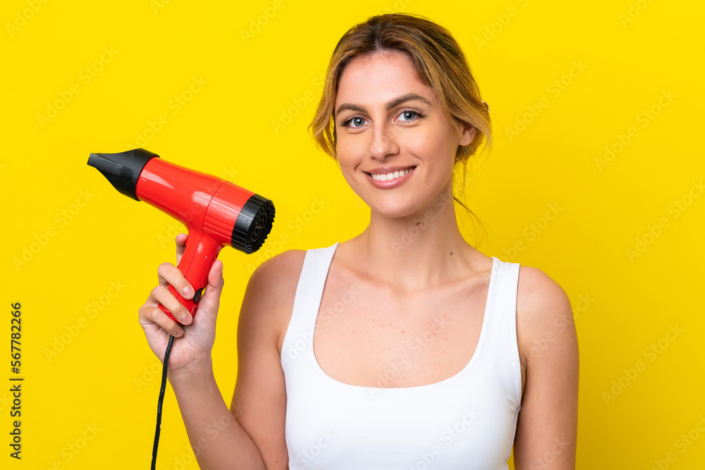 Young Uruguayan woman holding a hairdryer isolate don yellow background smiling a lot Young Uruguayan woman holding a hairdryer isolate don yellow background smiling a lot