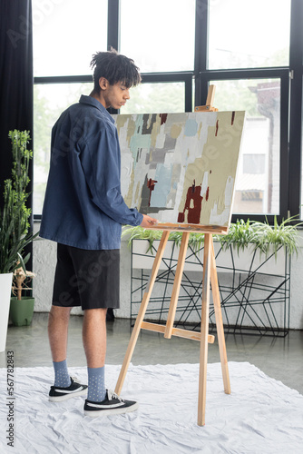Side view of young african american artist holding painting in workshop.