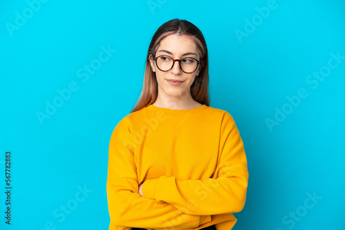 Young caucasian woman isolated on blue background having doubts while looking side