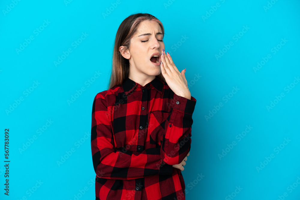 Young caucasian woman isolated on blue background yawning and covering wide open mouth with hand Young caucasian woman isolated on blue background yawning and covering wide open mouth with hand