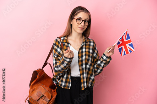 Young hispanic woman holding an United Kingdom flag isolated on pink background making money gesture