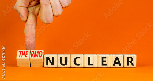 Nuclear or thermonuclear energy symbol. Concept words Nuclear or Thermonuclear on wooden cubes. Beautiful orange background. Businessman hand. Business Nuclear or thermonuclear concept. Copy space.