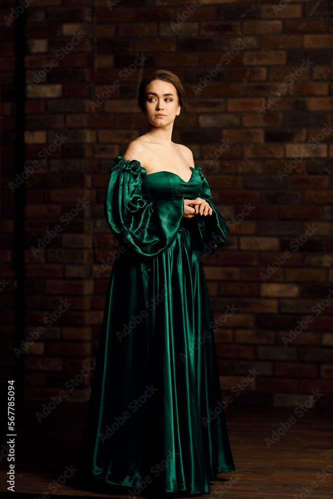 Full-length portraits of a girl in a green dress against a brown brick wall Full-length portraits of a girl in a green dress against a brown brick wall