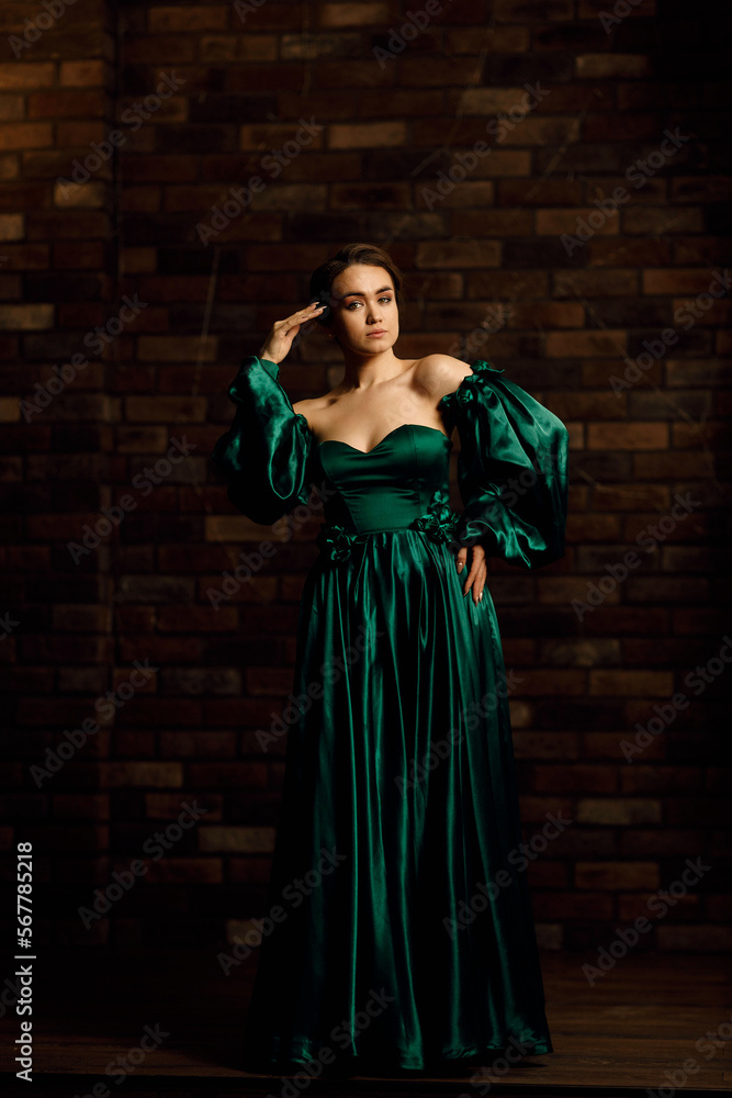 Full-length portraits of a girl in a green dress against a brown brick wall