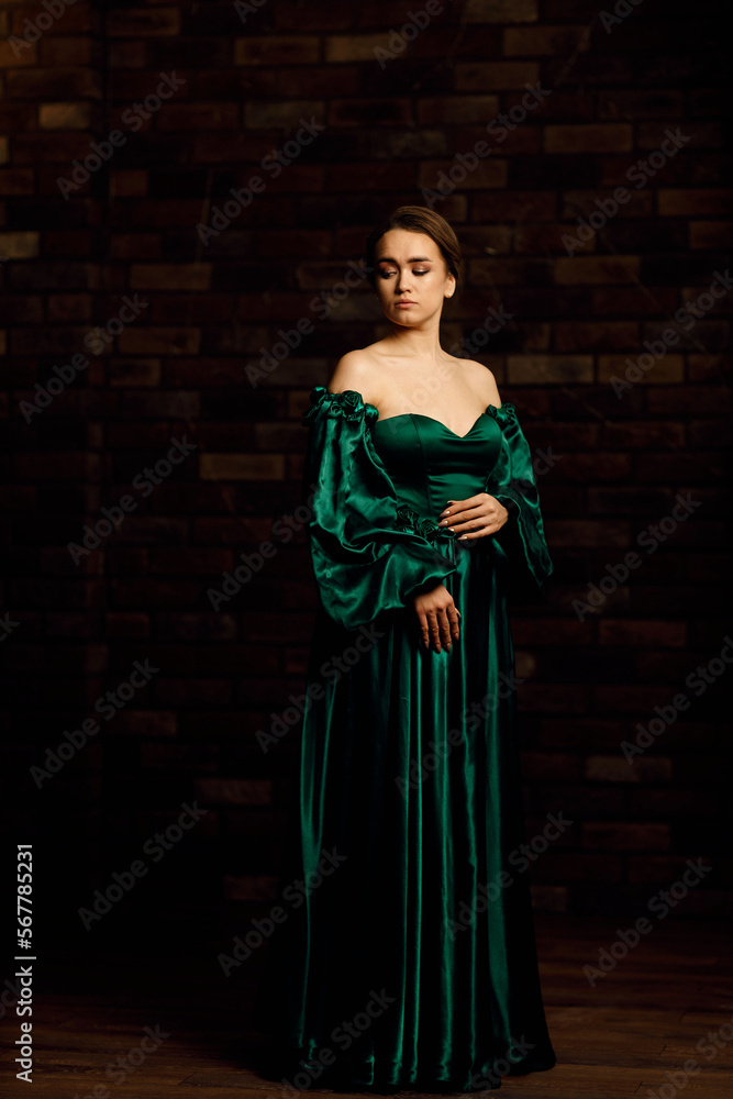 Fototapeta premium Full-length portraits of a girl in a green dress against a brown brick wall