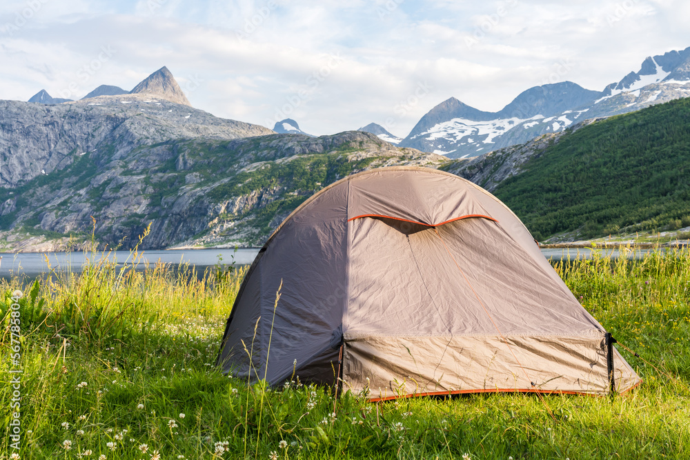 Tent in norwegian fjord landscape with snowcapped mountains in the background on a sunny summer day