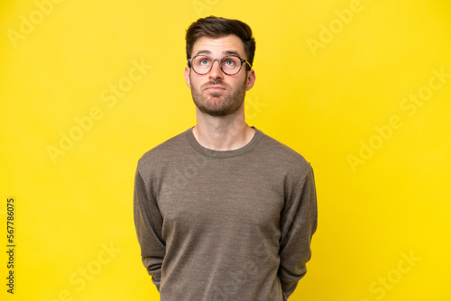 Young caucasian man isolated on yellow background and looking up