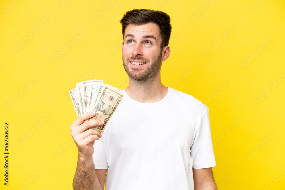 Young caucasian man taking a lot of money isolated on yellow background thinking an idea while looking up Young caucasian man taking a lot of money isolated on yellow background thinking an idea while looking up