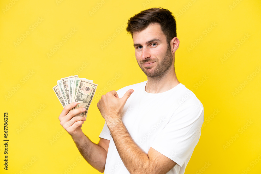 Young caucasian man taking a lot of money isolated on yellow background proud and self-satisfied Young caucasian man taking a lot of money isolated on yellow background proud and self-satisfied