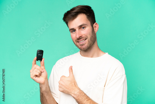 Young caucasian man holding car keys isolated on green background with thumbs up because something good has happened © luismolinero