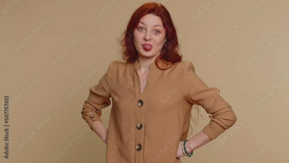 Cheerful funny bully redhead woman showing tongue making faces at camera, fooling around, joking, aping with silly face, teasing. Young ginger pretty girl isolated alone on beige studio background Cheerful funny bully redhead woman showing tongue making faces at camera, fooling around, joking, aping with silly face, teasing. Young ginger pretty girl isolated alone on beige studio background
