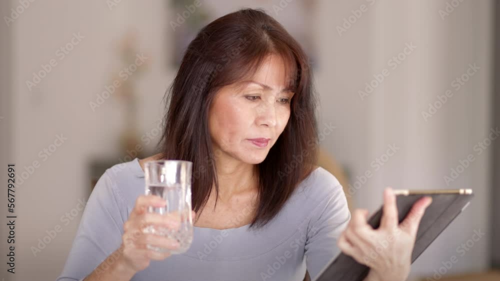 Smiling beautiful stylish woman relaxing reading mobile tablet story drinking glass of water sitting in comfortable chair at home