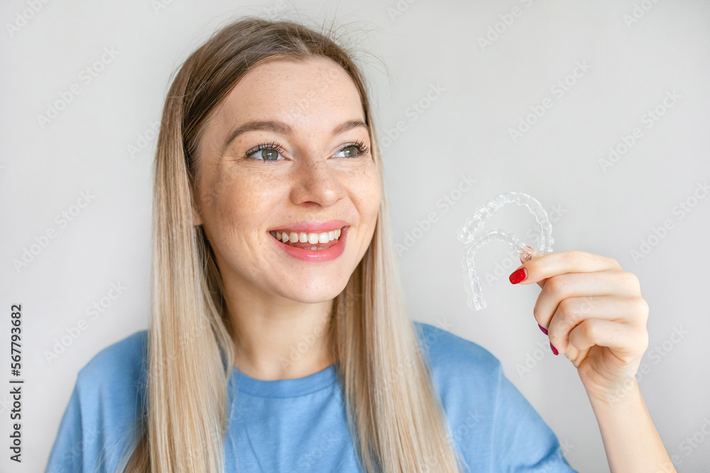 Beautiful smiling blonde woman is holding an invisible teeth aligner for orthodontic purposes. Includes copy space Beautiful smiling blonde woman is holding an invisible teeth aligner for orthodontic purposes. Includes copy space